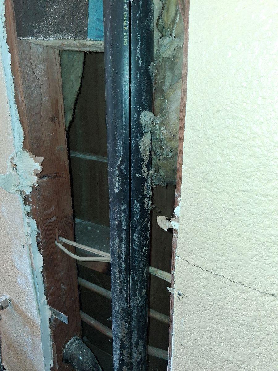 Cracked drain, waste and vent piping visible in an open laundry-room wall.